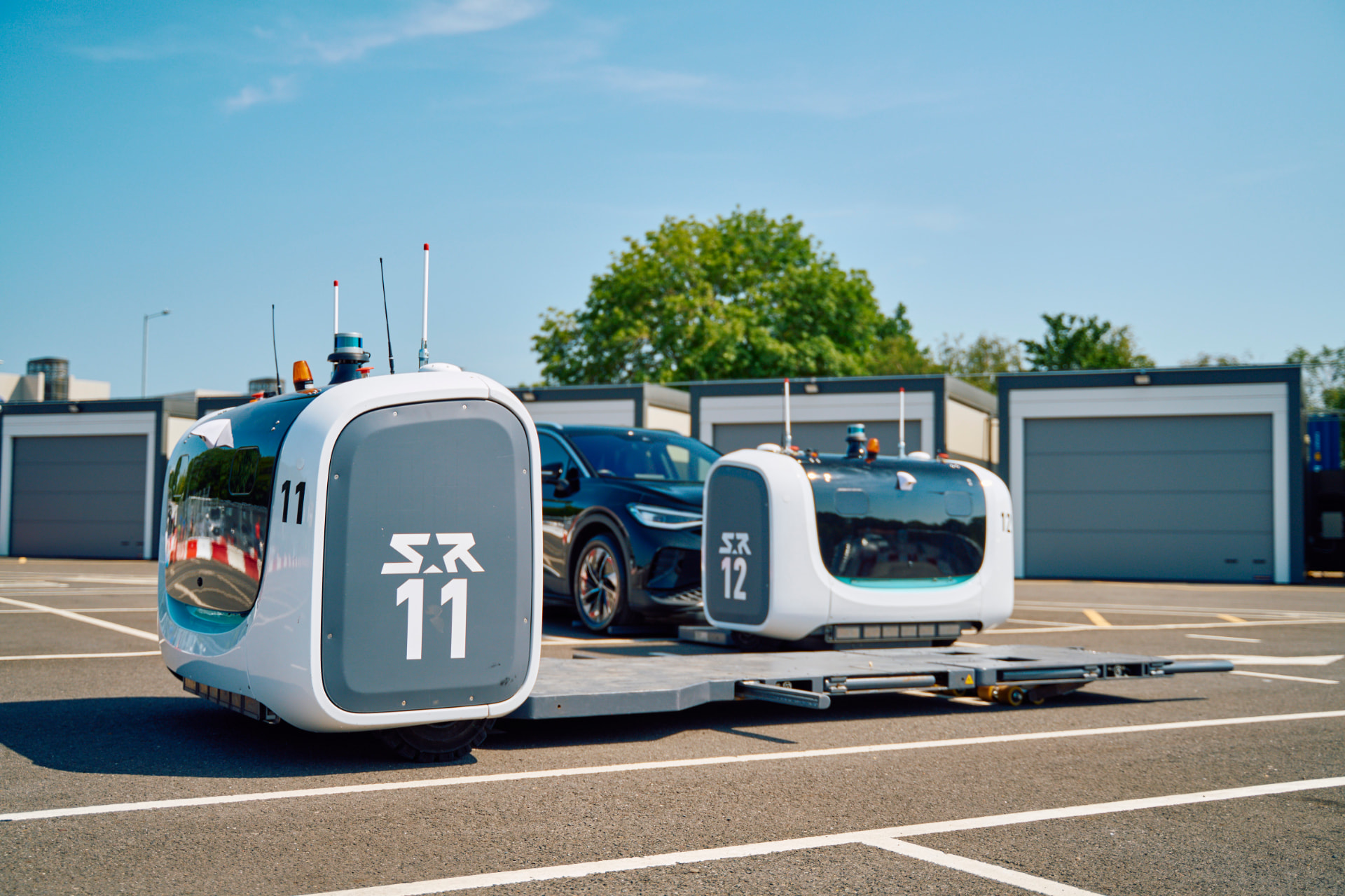 Two Stanley Robotics STAN robots carrying a passenger car across a parking site