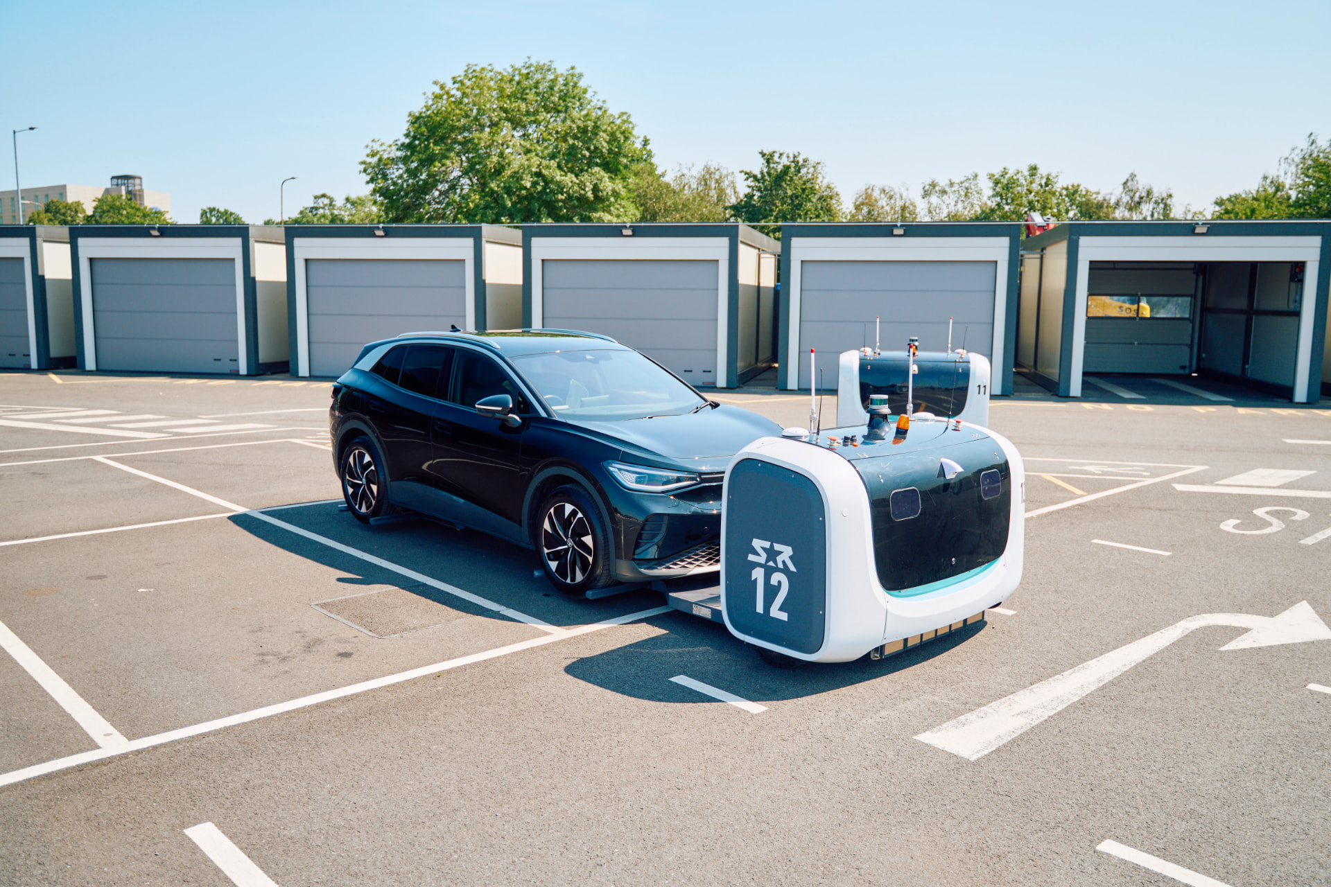 Two Stanley Robotics STAN robots carrying a dark electric SUV across a Gatwick parking bay
